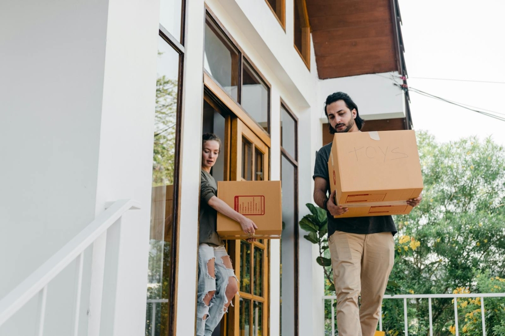 A young couple carrying boxes into their modern home, symbolizing moving day.